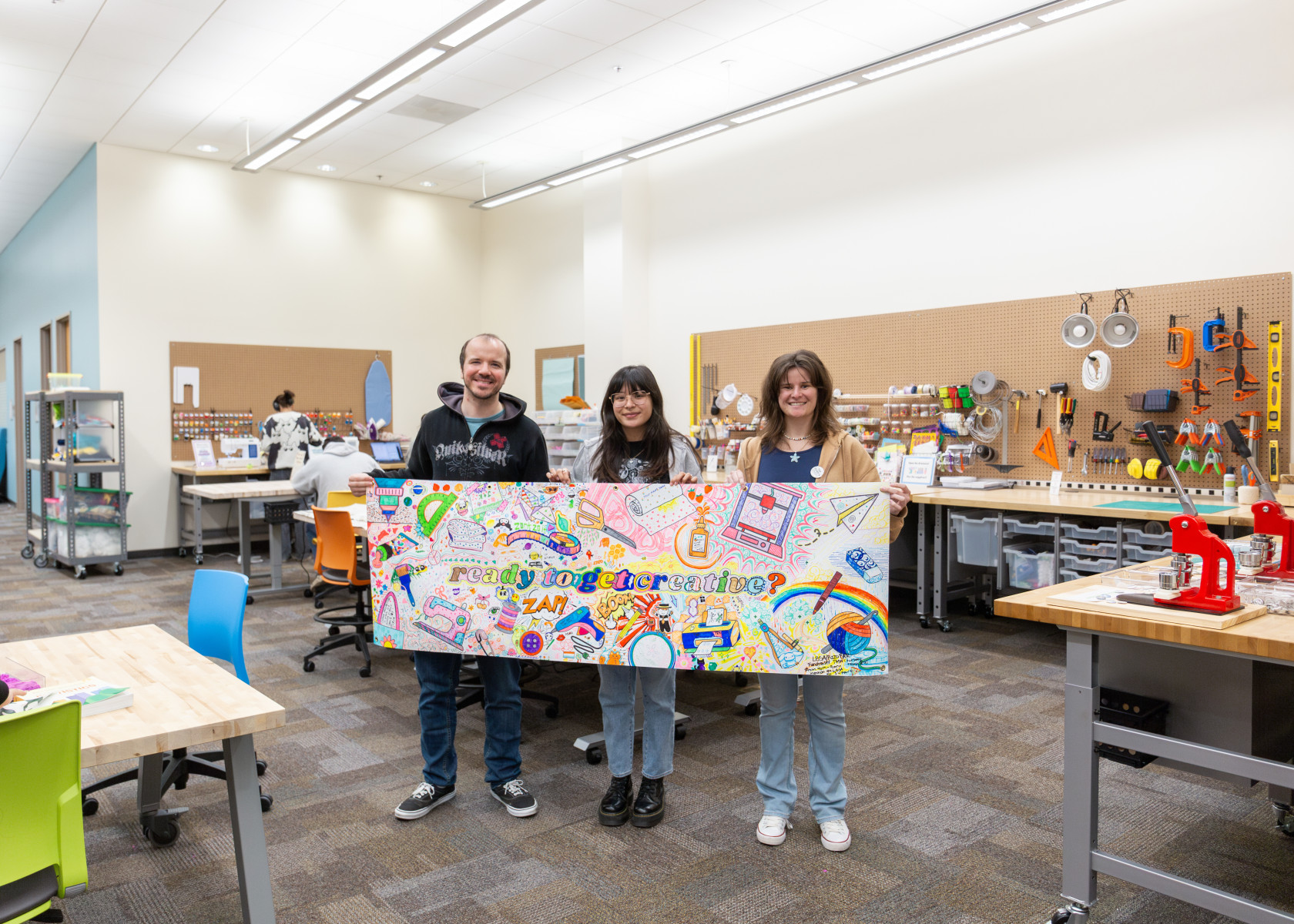 The Makery team members holding a coloring page banner that says, "ready to get creative?"