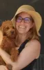 Woman wearing a hat and glasses, smiling, while holding her puppy, Daisy